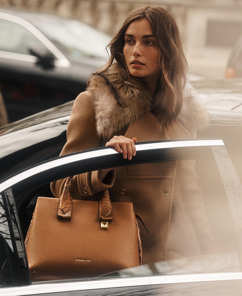 woman exits car while holding replica designer handbag