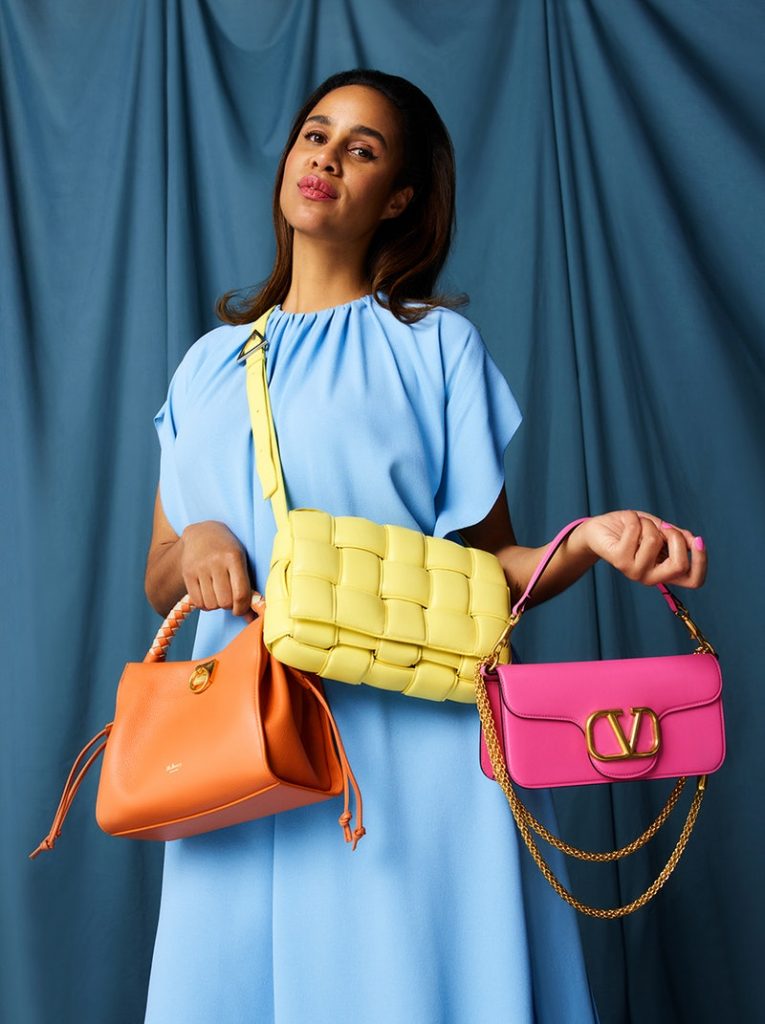 lady in blue dress holding her collection of knockoff designer bags including a Valentino Vring shoulder bag